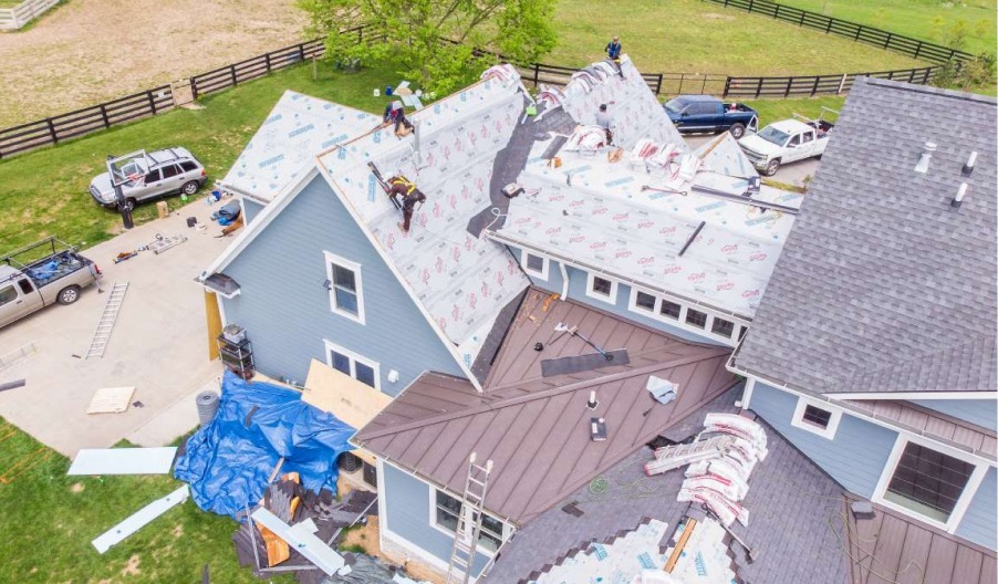Aerial view of roofing contractors replacing shingles on a house with shingle and tin roof.