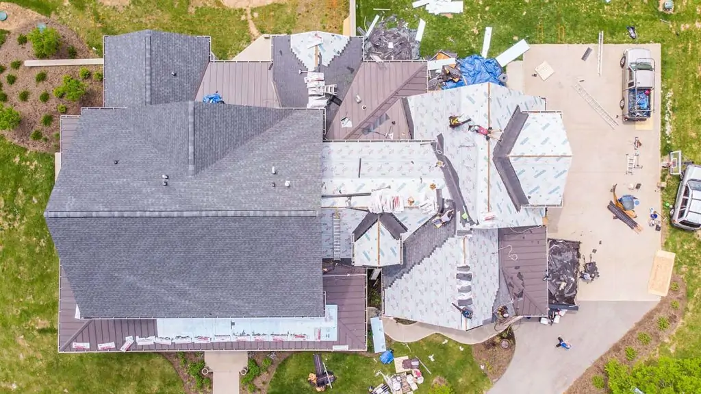Aerial view of roofing contractors completing roof replacement in Lexington Ky on the house with shingle and tin roof.