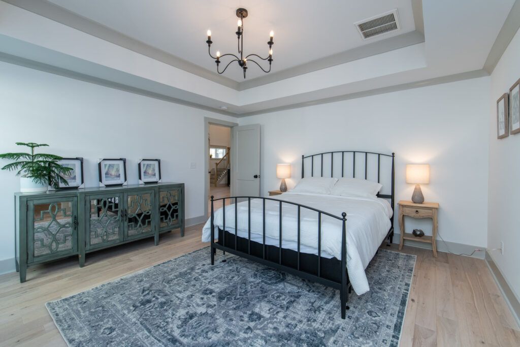 Bedroom with a tray ceiling, black iron bed, blue patterned rug, and a green mirrored cabinet
