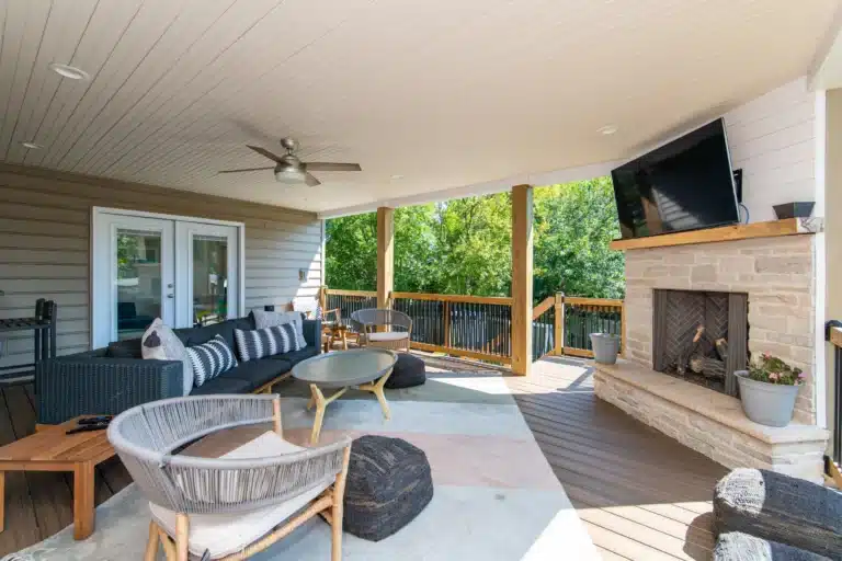 Covered deck living area in Lexington, KY with a stone fireplace, mounted TV, dark wicker sectional, and a round coffee table.