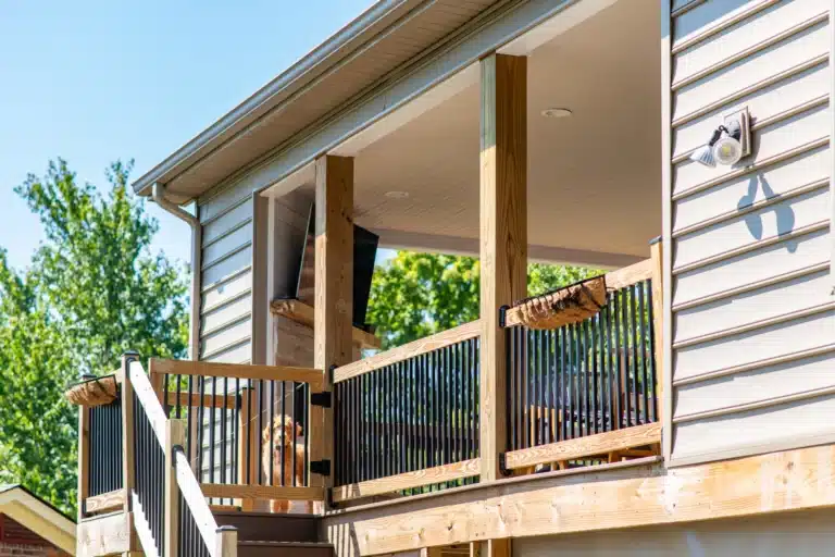 Close-up of a wood and black metal deck railing in Lexington, KY with a dog looking through the balusters, house siding in the background.